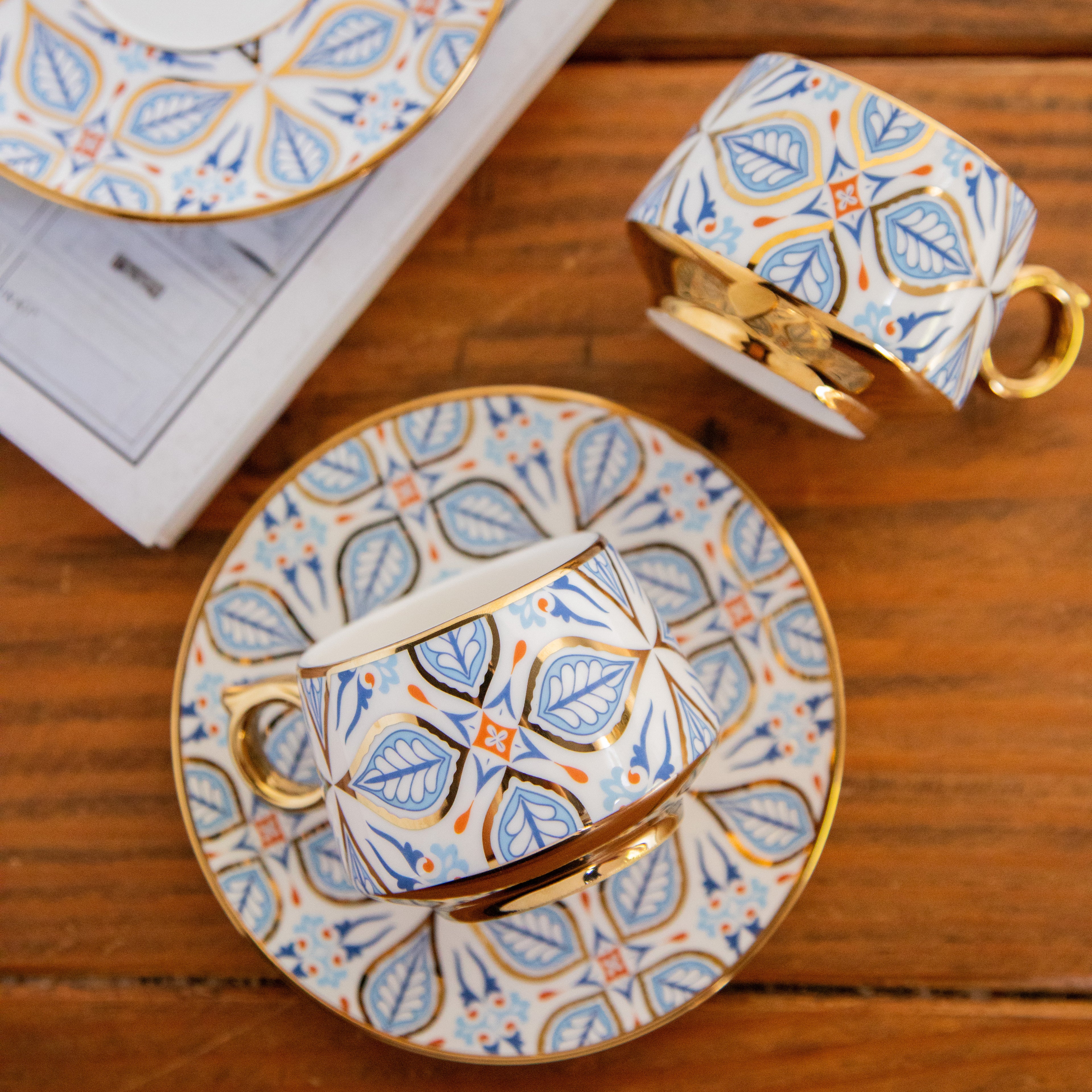 Decorative teacup and saucer set with intricate blue and orange pattern on a wooden surface.
